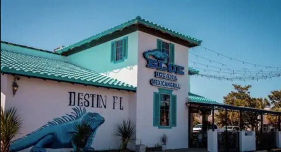 🌮 Taco Tuesday + Cinco de Mayo in Destin: The Best Mexican Restaurants Near Your Beach Condo | Beach Condos in Destin #White building with turquoise roof and shutters, a blue iguana mural, and signs for Destin, FL and Blue Iguana Mexican Grill under string lights.