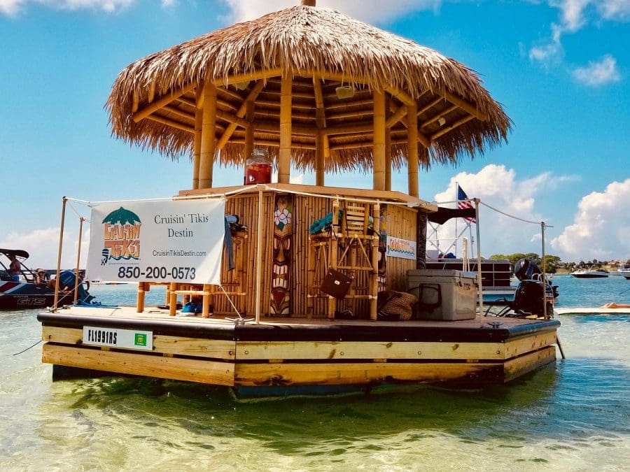 Watersport Activities in Destin | Beach Condos in Destin #Floating tiki bar on clear water with thatched roof and banner reading 'Cruisin' Tikis Destin' and contact number 850-200-0573