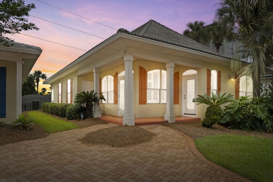 1-web-or-mls-FDP00940 | Beach Condos in Destin Beach Condos in Destin FL | Vacation Rentals Online #A beige bungalow with white columns, orange shutters, and a tiled roof at sunset.