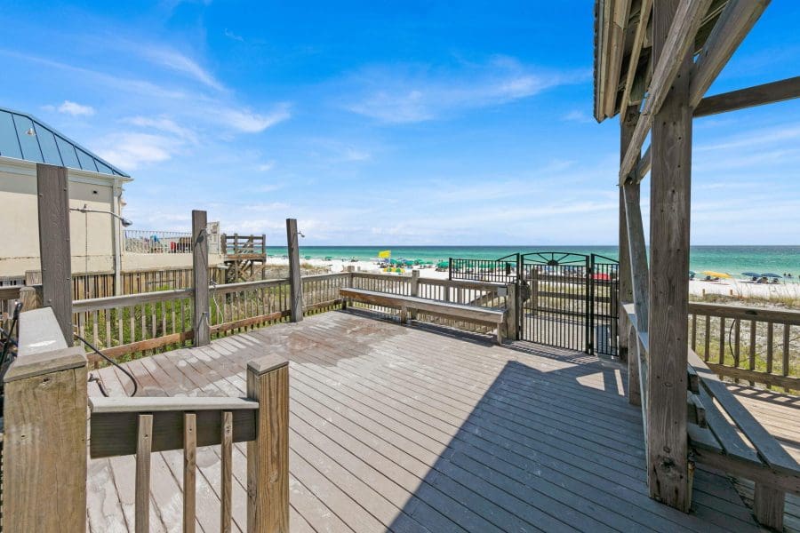 Emerald Shores | Beach Condos in Destin #Wooden beach deck with railings overlooking a sunny beach and turquoise ocean under a blue sky.