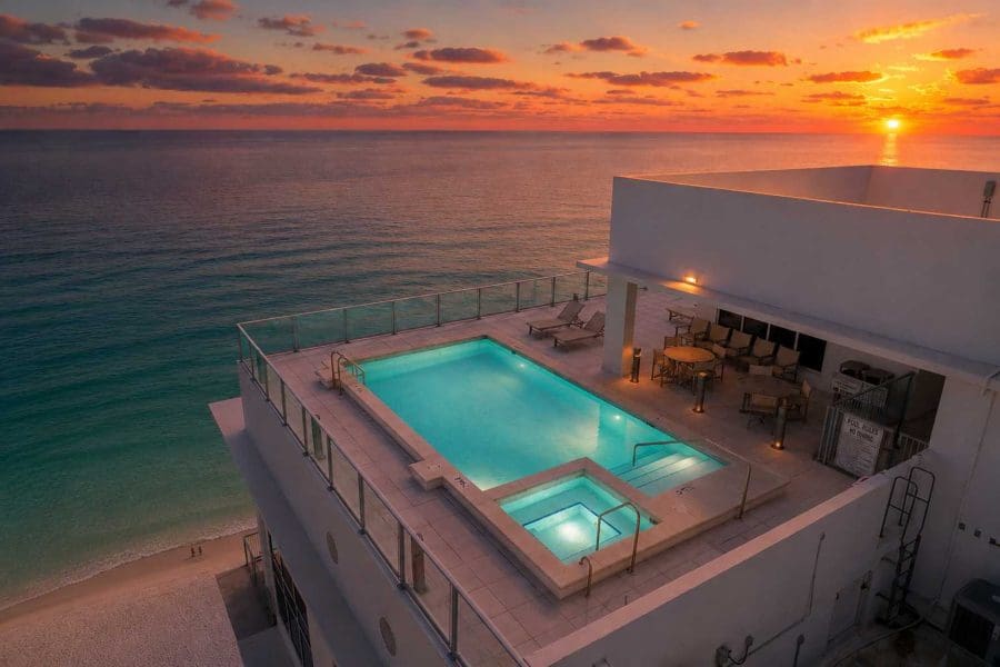 Rooftop-pool-with-panoramic-gulf-views-1900-98_1535w | Beach Condos in Destin 1900 Ninety Eight | Beach Condos in Destin #Rooftop pool on a white building overlooking the ocean at sunset, with lounge chairs and a seating area along the deck.