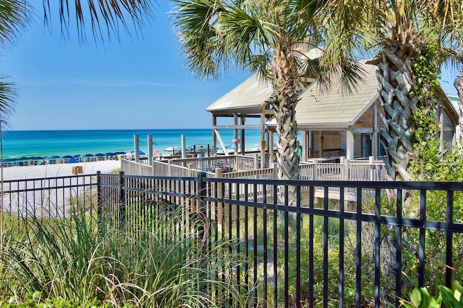 Emerald Shores | Beach Condos in Destin #Beachside pavilion and deck with chairs by the turquoise ocean, palm trees in the foreground.